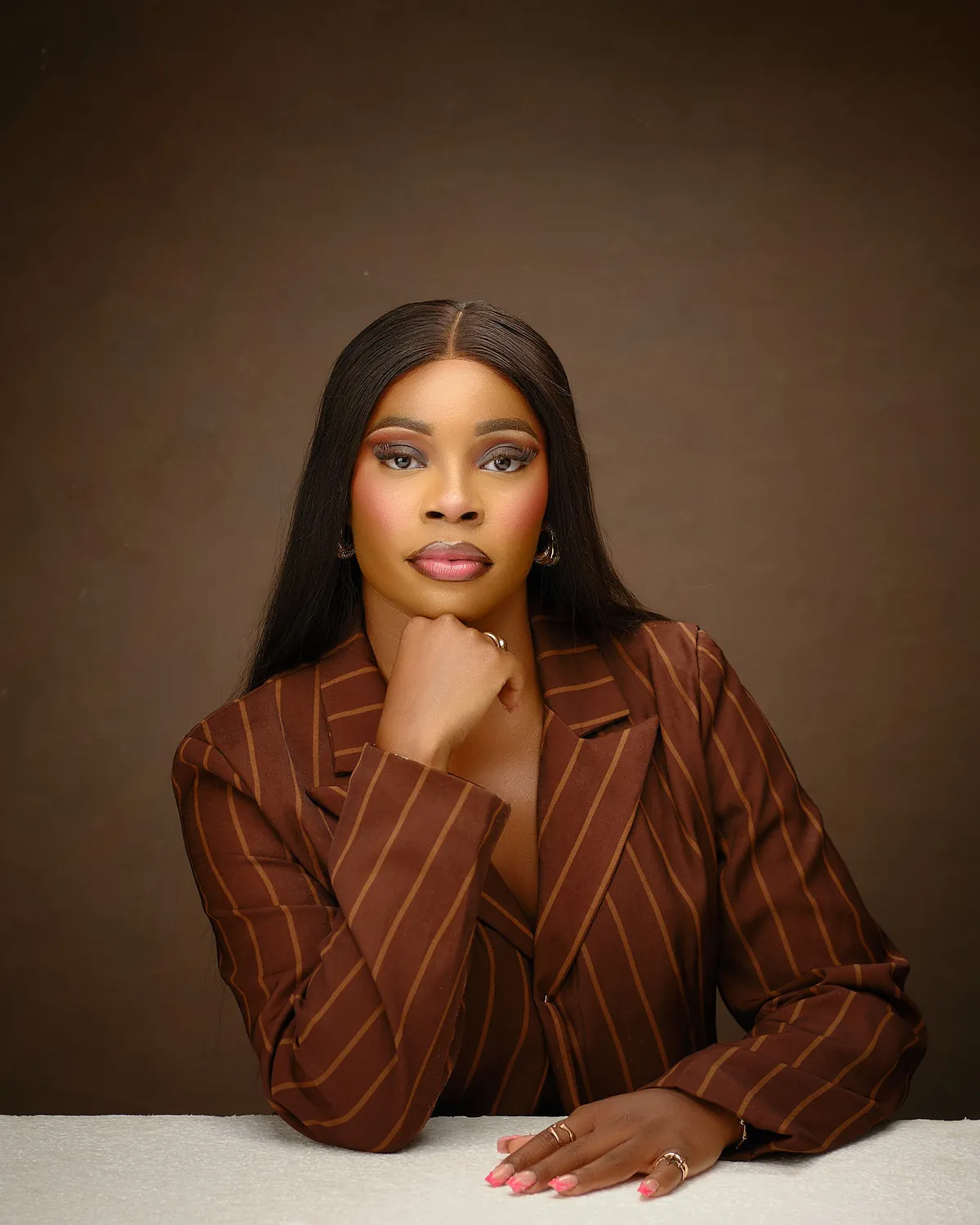 Achiever Omoobajesu resting her chin on her hand, in a brown pinstripe blazer